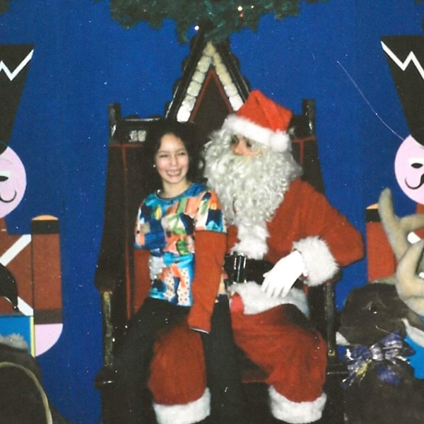 Une fillette souriante assise sur les genoux d'un Père Noël, sur fond de décor festif bleu