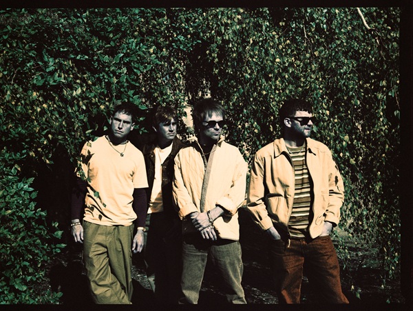 Les quatre membres d'Enter Shikari posant en extérieur, devant une haie verdoyante