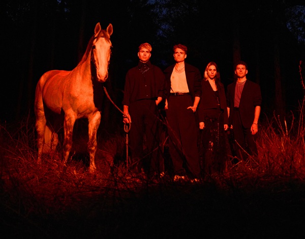 Le groupe Daytime TV posant avec un cheval dans une forêt nocturne, éclairé par une lumière rouge-orangée