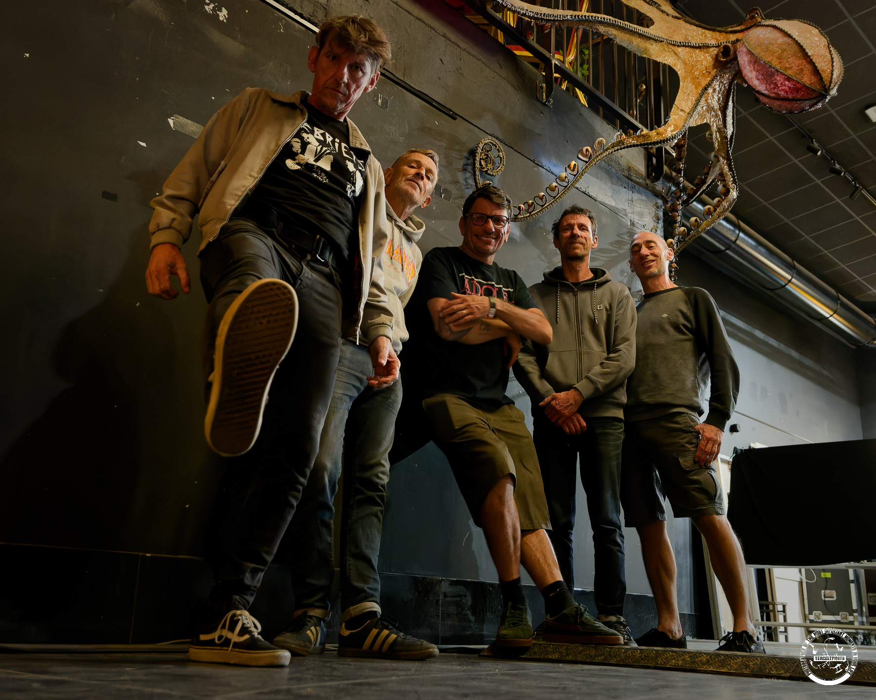 Les cinq membres des Burning Heads posant sur une scène, sous une grande sculpture de pieuvre