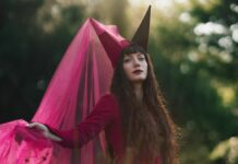 Annicke Shireen dévoile « False Gods » avant son album DELIRIUM Annicke Shireen en robe rouge, coiffée d'un chapeau pointu, avec un voile rose flottant au vent dans un décor forestier