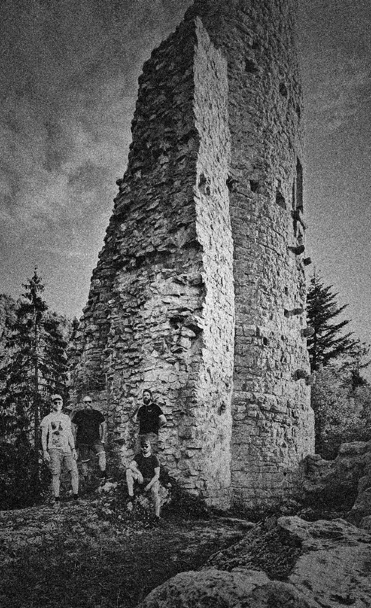 Photo en noir et blanc des membres de Love Sex Machine au pied d'une tour en ruine