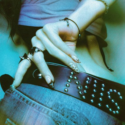 Gros plan sur une main aux ongles longs et bagues, posée sur une ceinture cloutée