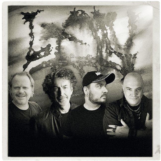 Photo promotionnelle en noir et blanc de quatre musiciens devant un décor abstrait sombre