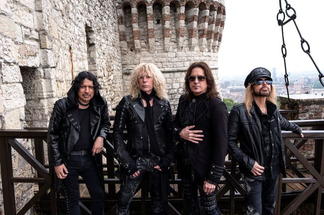 Les membres de Stryper posant sur les remparts d'un château, avec une ville en arrière-plan