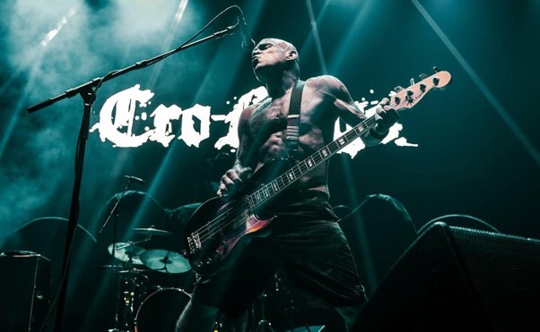 Le chanteur des Cro-Mags sur scène, sous les lumières bleutées, avec le logo du groupe en arrière-plan