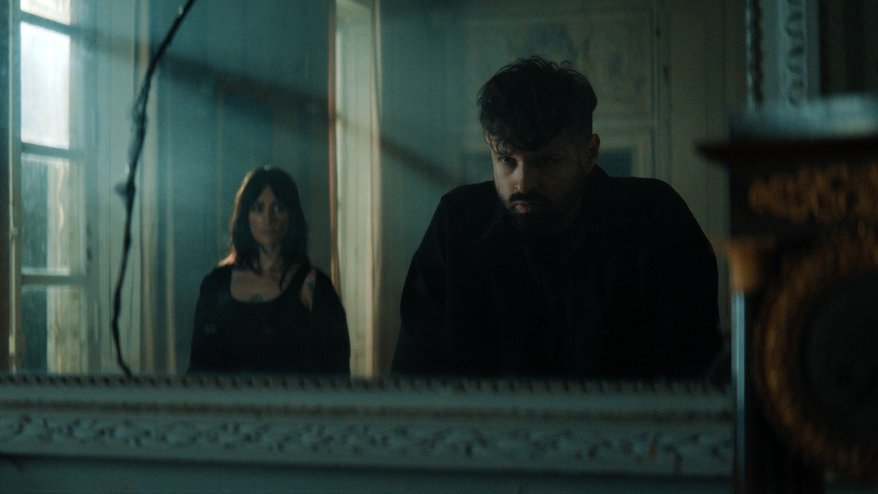 Un homme et une femme photographiés à travers une fenêtre, dans un intérieur sombre