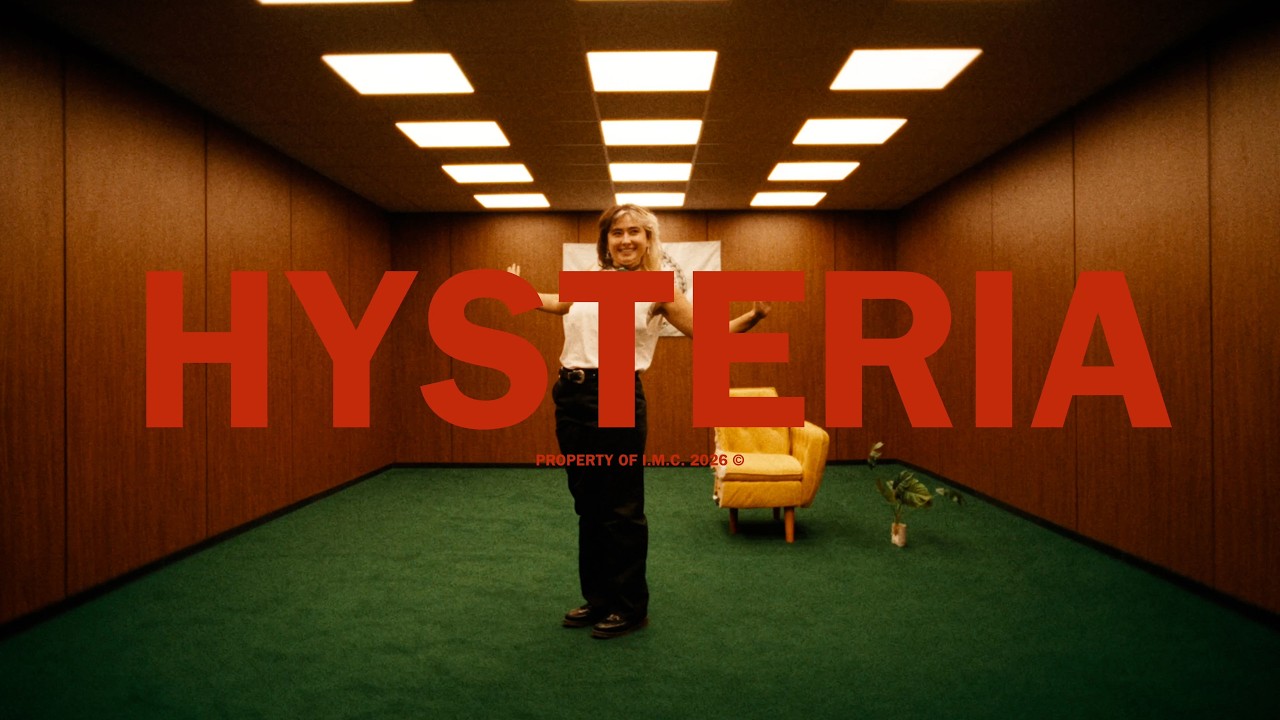Image du clip « Hysteria » : une personne au centre d'une pièce aux murs en bois, au sol vert, avec le titre HYSTERIA en rouge