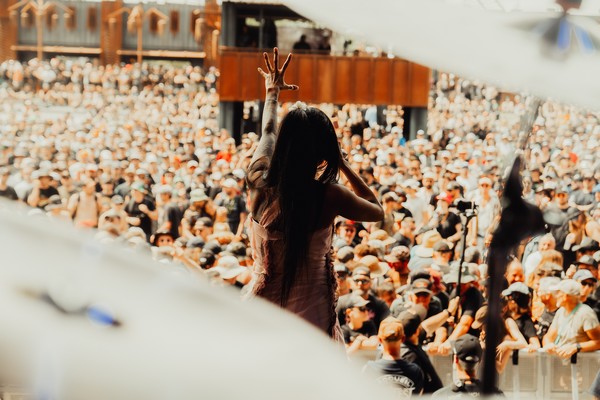 Une chanteuse de dos, bras levés, face à une foule immense lors d'un concert en plein air